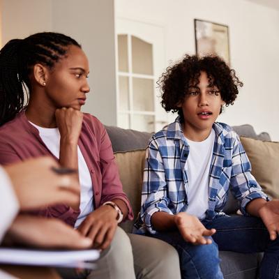 A boy sitting next to his mother in discussion with a doctor in a living room during a home visit.